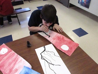 A student uses a straw to direct air on ink to create a tree-like shape. (Photo submitted)