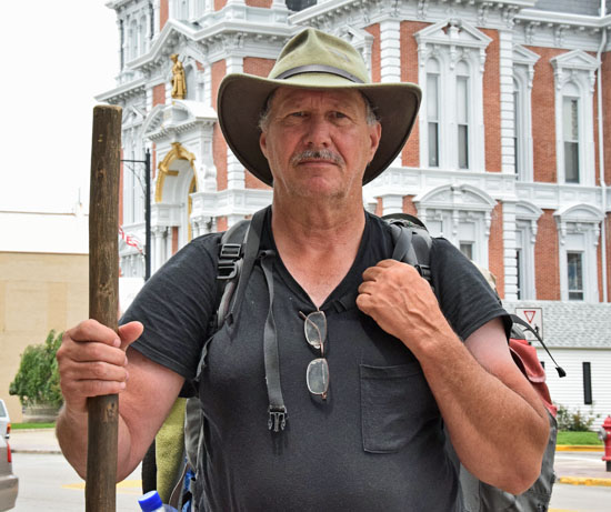 Cross-country walker Steve Young poses with his walking stick and pack in front of the Van Wert County Courthouse. (Dave Mosier/Van Wert independent)