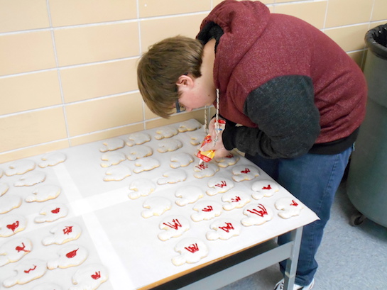 As part of Homecoming Spirit Week, LifeLinks Community School baked and decorated football helmet shaped cookies for the team and coaches.   Shown is Chance Mowery using his incredible artistic abilities to decorate each cookie with a red VW on a gray helmet. (Photo submitted.)