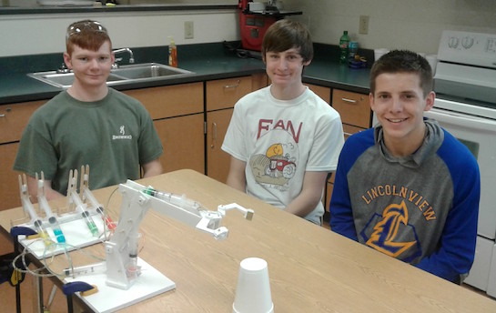 As part of the Principles of Engineering course, Taylor Braun (12), Chayten Overholt (11), and Jacob Keysor(10) constructed a hydraulic powered mechanical arm from styrofoam board, tongue depressors, syringes, and other ordinary materials.  The class applied concepts from chemistry (Ideal Gas Laws) and physics (Pascal's Principle) in studying pneumatics and hydraulics.  The mechanical arm can be either a pneumatic or hydraulic device.  (Photo submitted.)